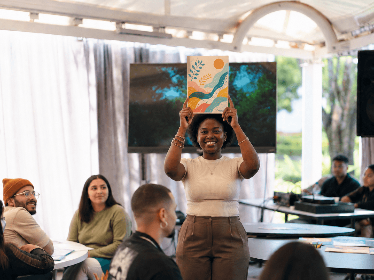 A young woman smiling as she holds up the artwork she made at a Heyrafiki session